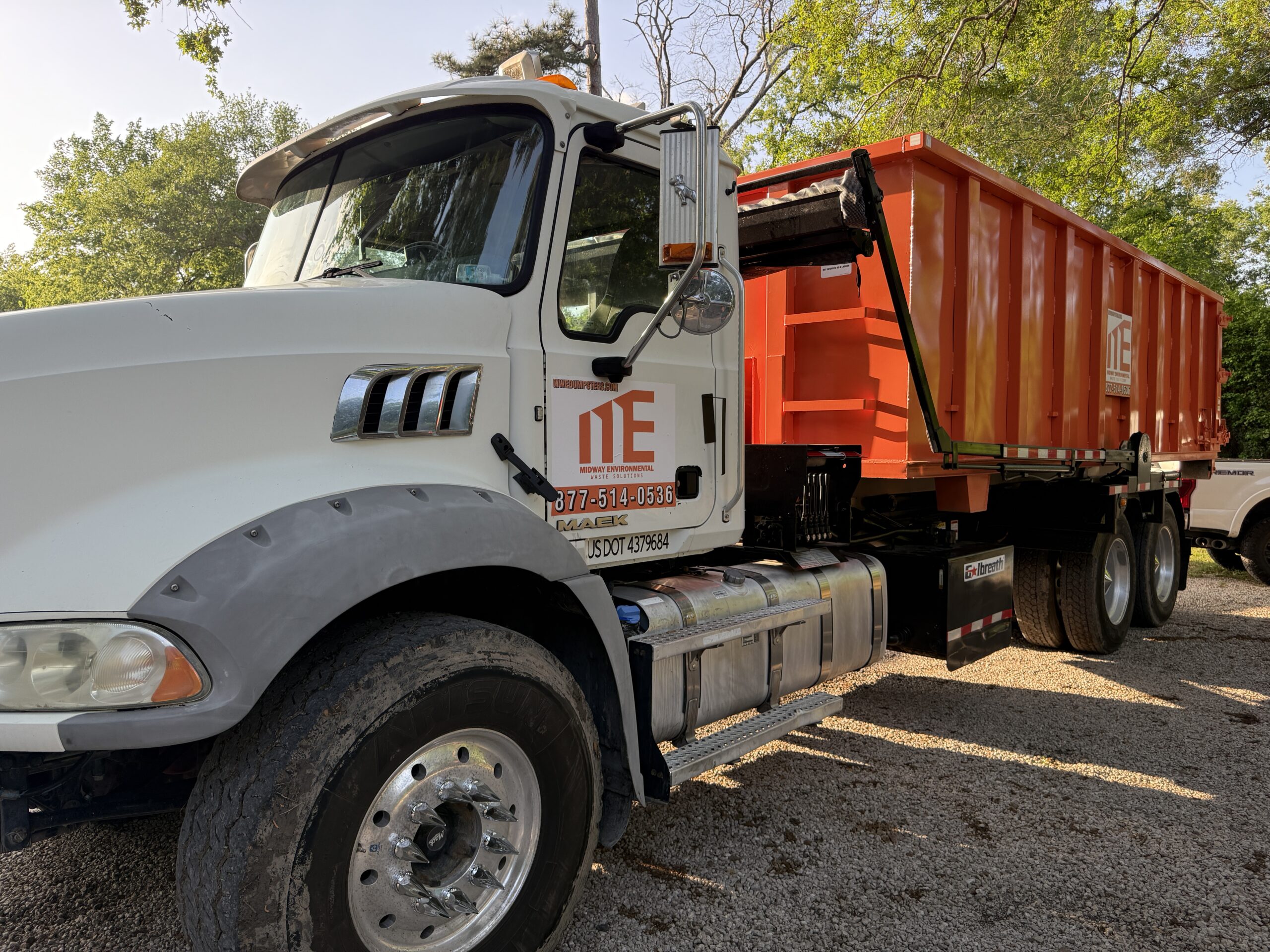 White semi-truck with orange trailer parked outdoors near trees.
