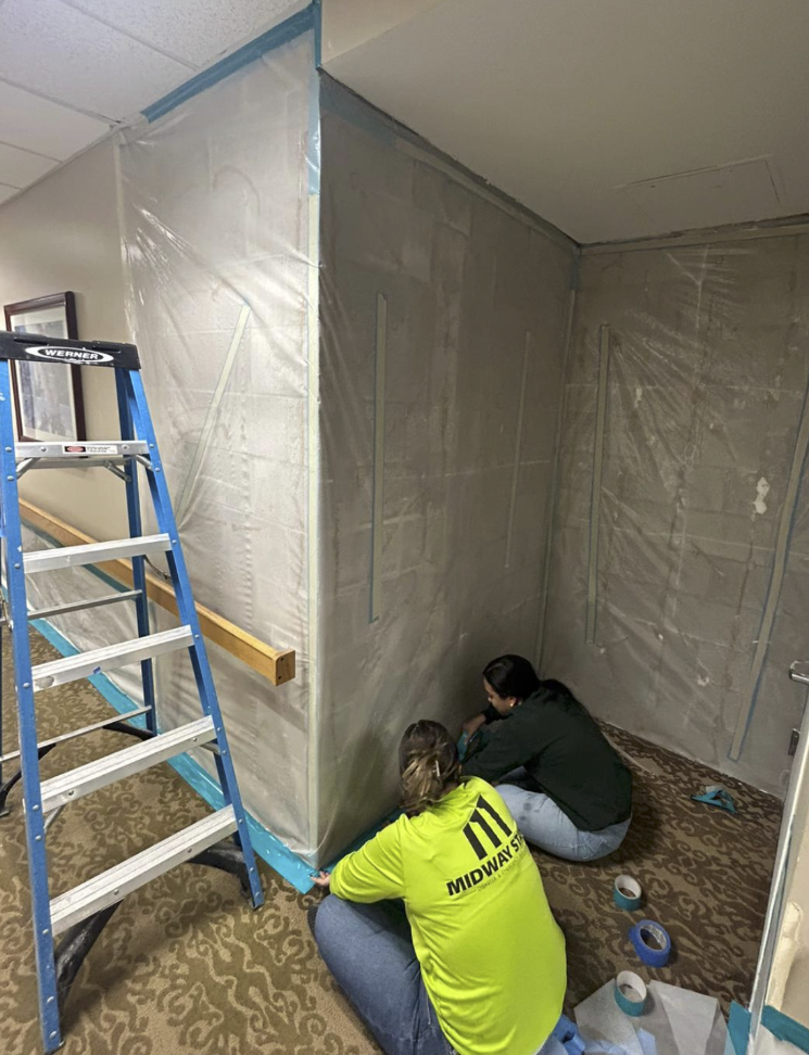 Two workers installing wall panels in a room under construction.