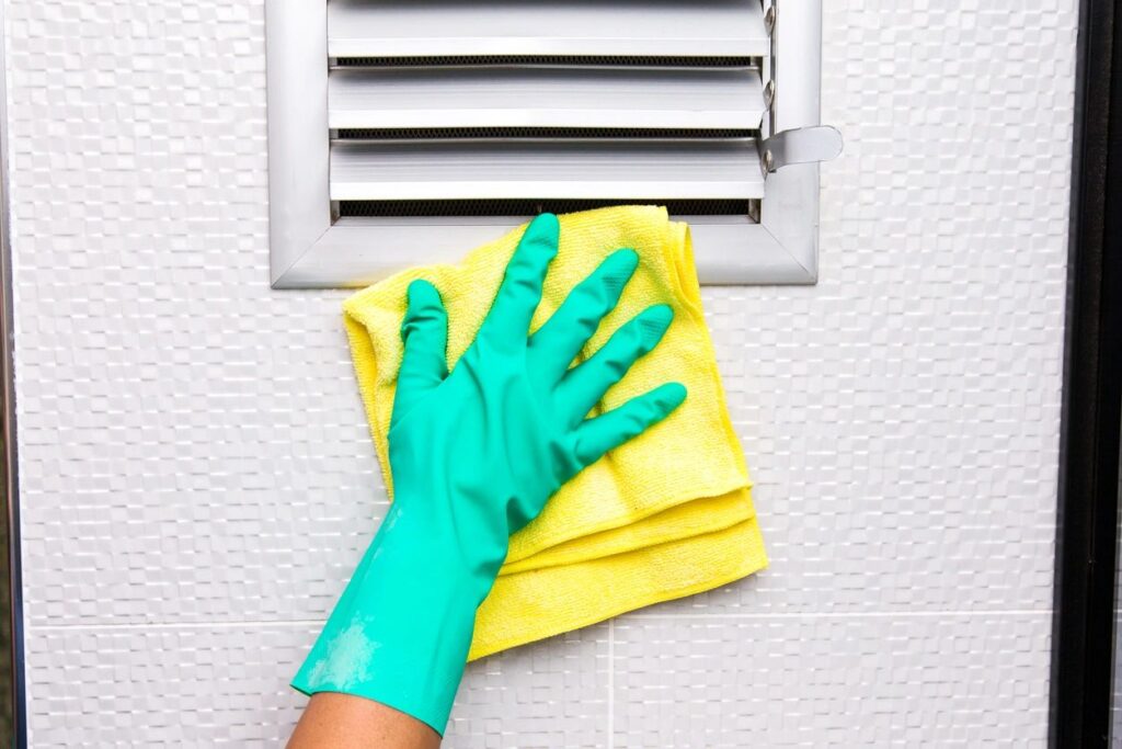 Hand in green glove wiping surface with yellow cloth.