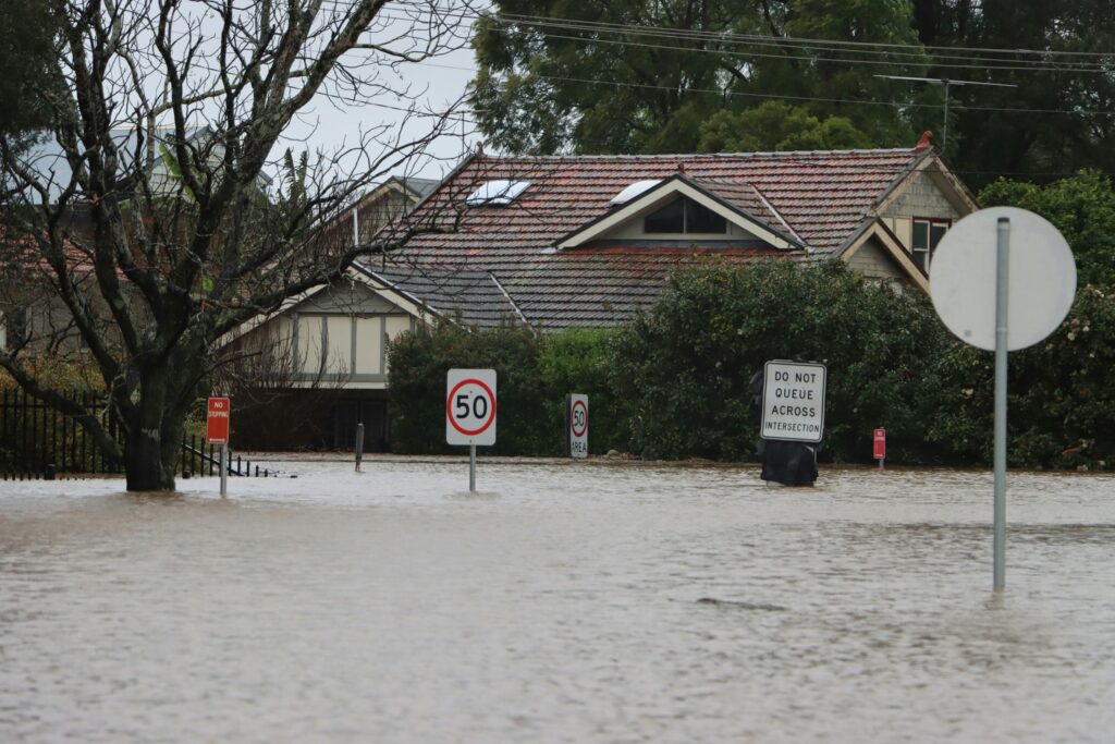 Flooded street with warning signs and a house in the background.